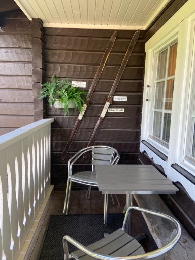 Balkong med ett bord, två stolar och grön växt på väggen.